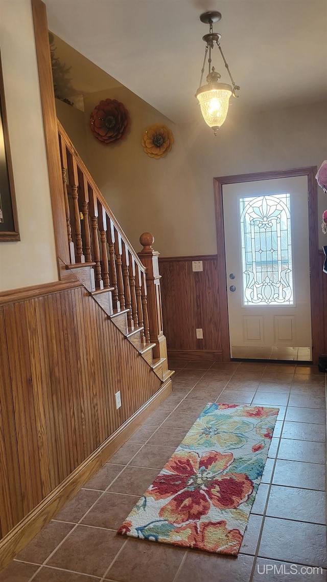 tiled entryway with wood walls, stairway, and wainscoting