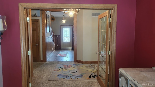 doorway with visible vents, baseboards, tile patterned flooring, carpet flooring, and a notable chandelier