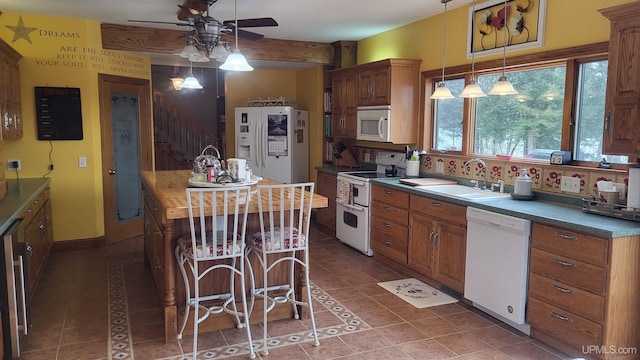 kitchen featuring white appliances, dark tile patterned floors, a sink, brown cabinets, and dark countertops