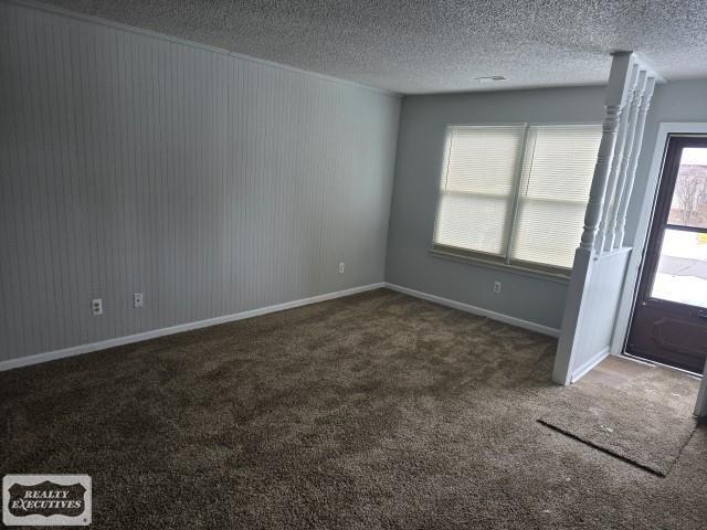 empty room featuring dark carpet, a textured ceiling, and baseboards