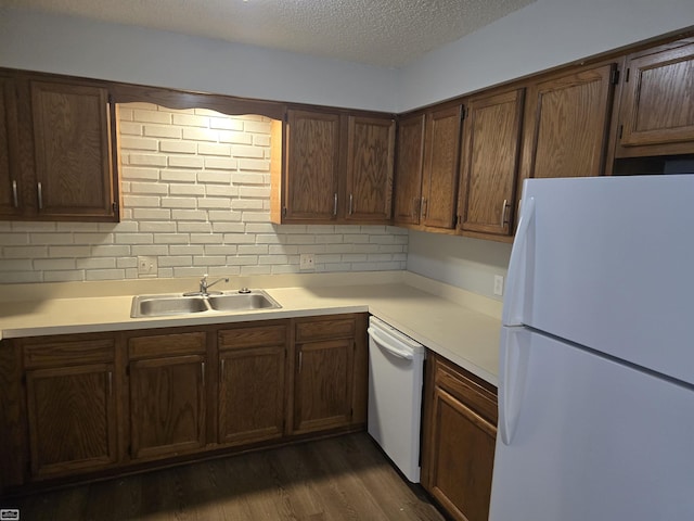 kitchen with a textured ceiling, light countertops, white appliances, and a sink