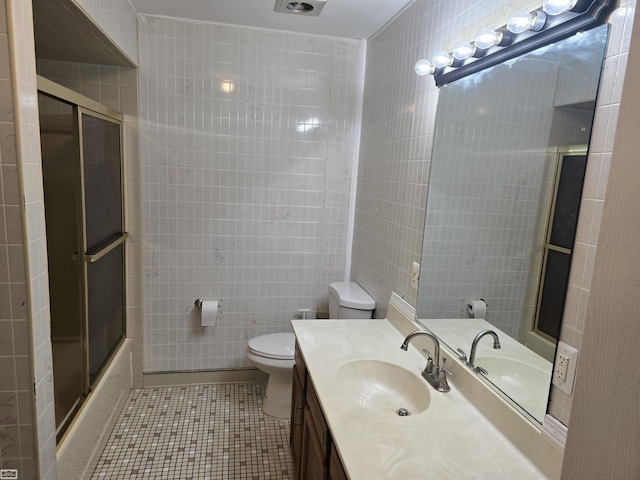 bathroom with tile walls, toilet, enclosed tub / shower combo, vanity, and tile patterned flooring