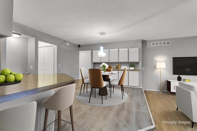 dining space with light wood-type flooring, baseboards, and visible vents