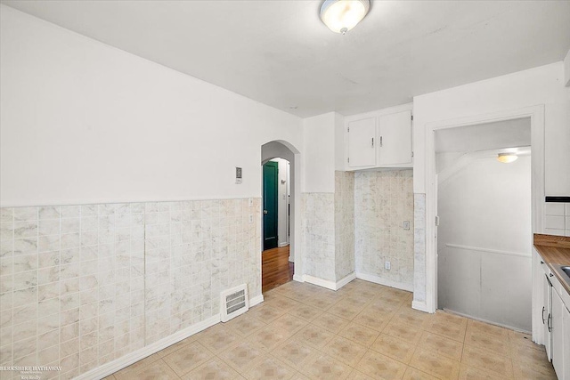 interior space featuring arched walkways, a wainscoted wall, visible vents, and tile walls