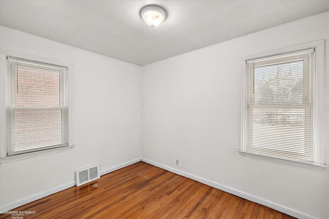 unfurnished room with baseboards, visible vents, and wood finished floors