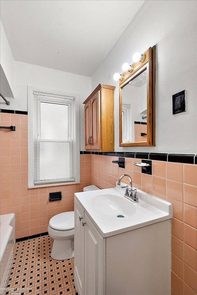 full bath featuring vanity, tile walls, toilet, and wainscoting