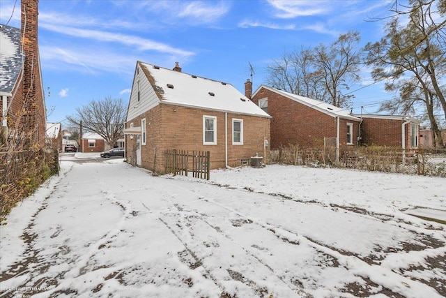 snow covered rear of property featuring central AC unit, a chimney, fence, and brick siding