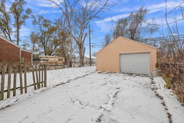 snow covered garage with a detached garage and fence