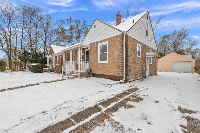 view of snowy exterior with a garage, stone siding, an outdoor structure, and a chimney