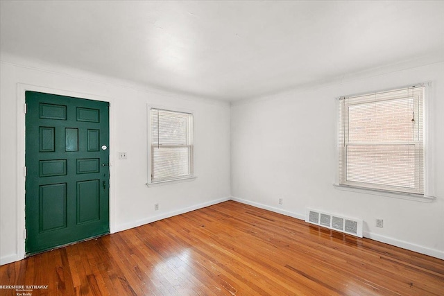 empty room featuring hardwood / wood-style floors, a healthy amount of sunlight, visible vents, and baseboards