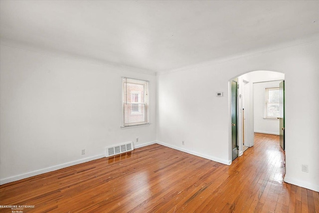 spare room featuring wood-type flooring, visible vents, arched walkways, and baseboards