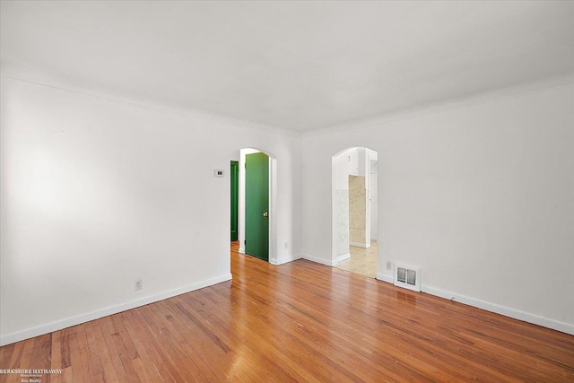 spare room with light wood-style floors, visible vents, arched walkways, and baseboards