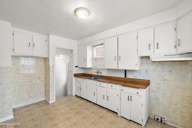 kitchen featuring dark countertops, a sink, white cabinets, under cabinet range hood, and tile walls