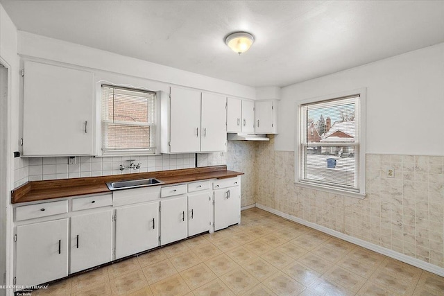 kitchen with a wainscoted wall, white cabinetry, and a sink