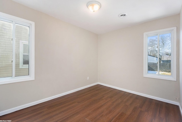 empty room featuring dark wood-style floors, visible vents, and baseboards