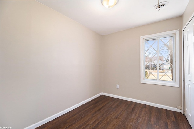 spare room featuring dark wood-type flooring, visible vents, and baseboards