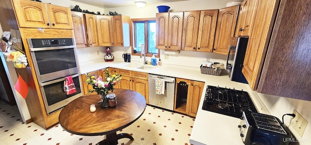 kitchen featuring stainless steel appliances, a sink, light countertops, light floors, and brown cabinetry