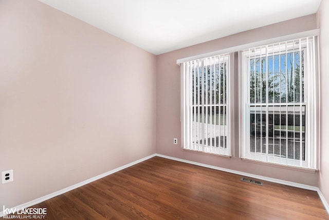 empty room featuring baseboards, wood finished floors, visible vents, and a healthy amount of sunlight