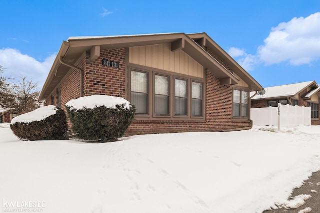 view of snow covered exterior with brick siding and fence