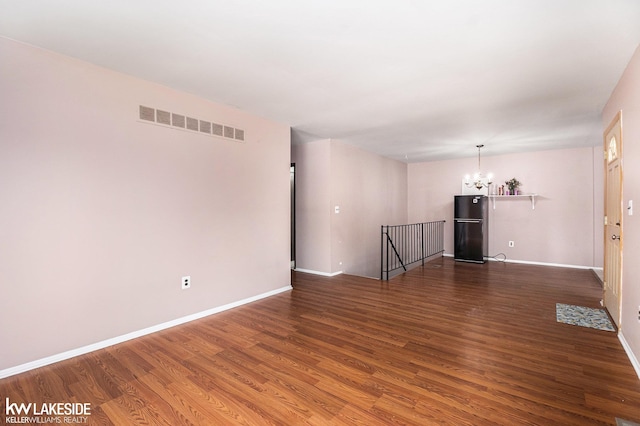 empty room with baseboards, dark wood-type flooring, visible vents, and an inviting chandelier