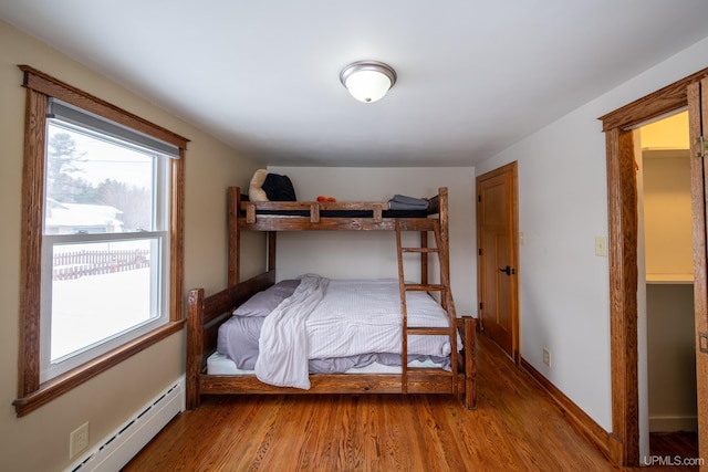 bedroom with baseboard heating, wood finished floors, and baseboards