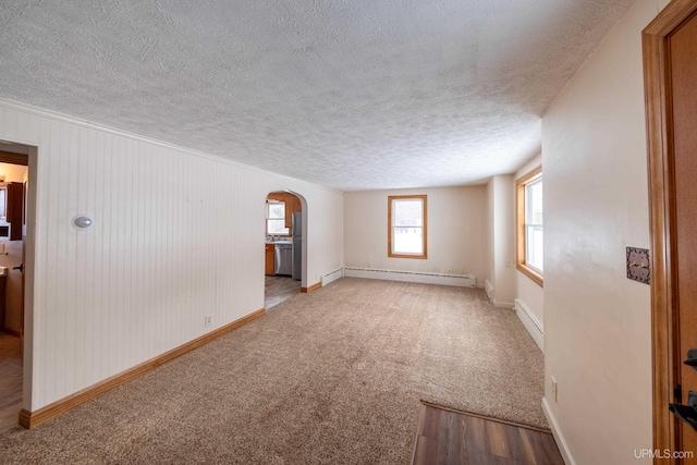 carpeted empty room with baseboards, arched walkways, a baseboard radiator, baseboard heating, and a textured ceiling