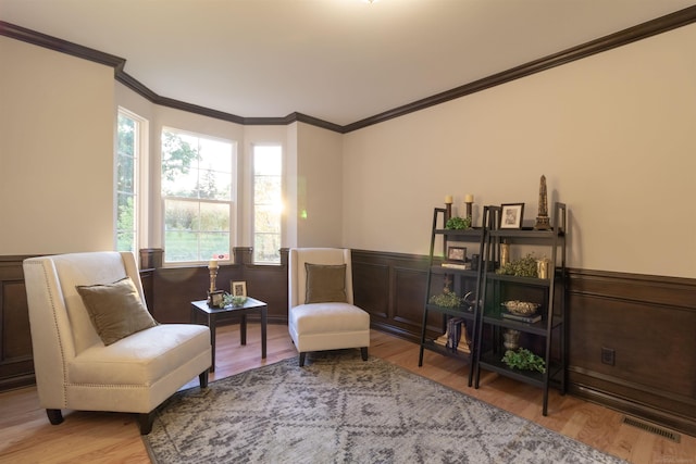 sitting room with light wood-style floors, a wainscoted wall, and crown molding