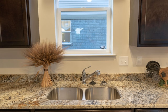 room details featuring a sink, dark brown cabinets, and light stone countertops