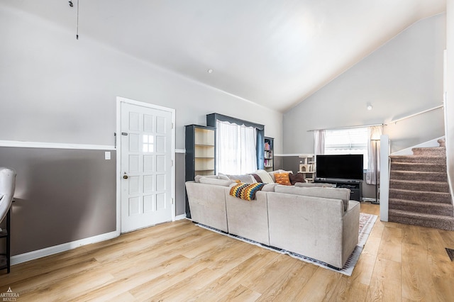 living room featuring high vaulted ceiling, baseboards, stairway, and light wood finished floors