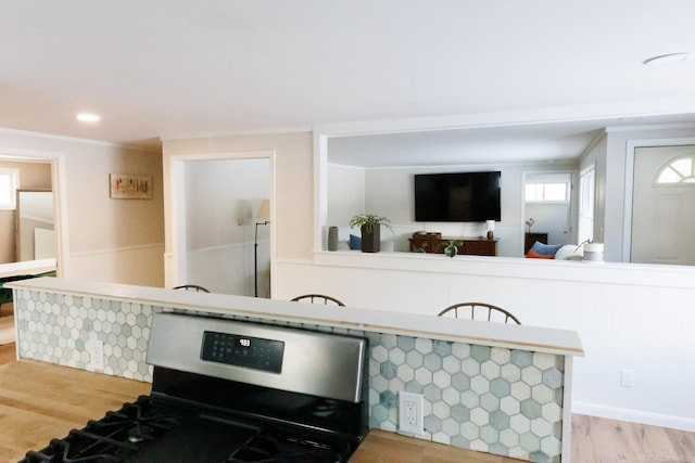 kitchen with ornamental molding, a peninsula, stainless steel gas range oven, and light wood-style flooring