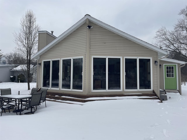 snow covered rear of property featuring a chimney