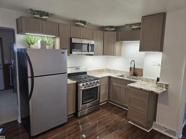 kitchen featuring light stone counters, appliances with stainless steel finishes, a sink, and dark wood finished floors