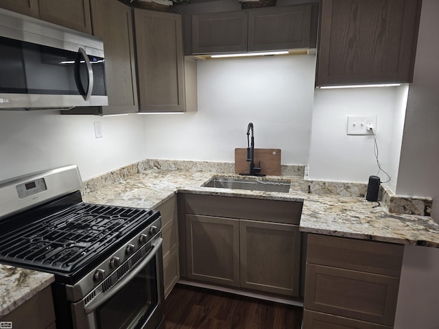 kitchen with light stone counters, stainless steel appliances, dark wood-style flooring, a sink, and dark brown cabinets