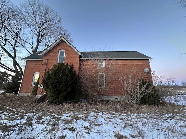 view of snowy exterior with brick siding, crawl space, and a shingled roof