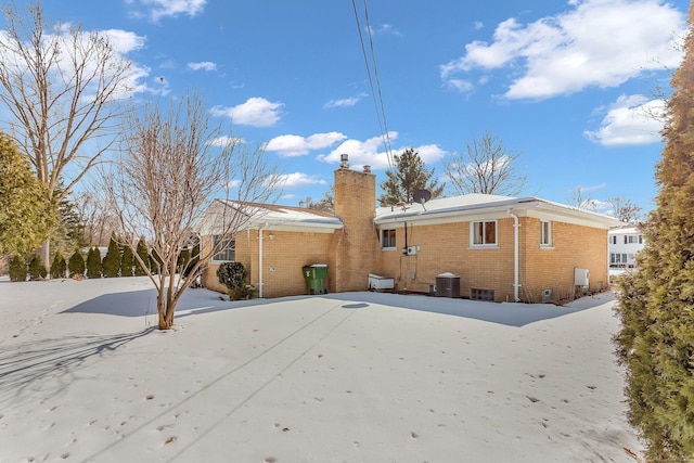 back of property featuring brick siding, a chimney, and central AC unit