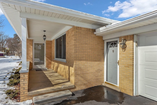 snow covered property entrance with a garage and brick siding