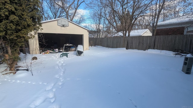 yard layered in snow with a garage, an outbuilding, and fence