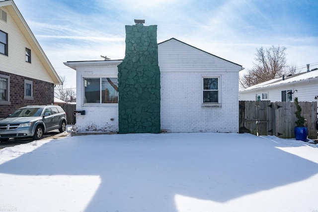 view of snowy exterior with brick siding, fence, and a chimney