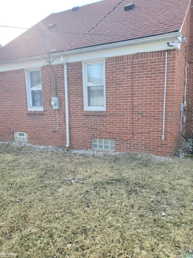 view of side of home with a yard, a shingled roof, and brick siding