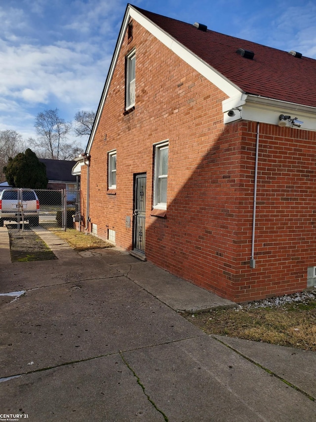 view of side of home featuring brick siding and a gate