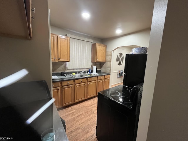 kitchen with light wood-style floors, dark countertops, a sink, black appliances, and backsplash