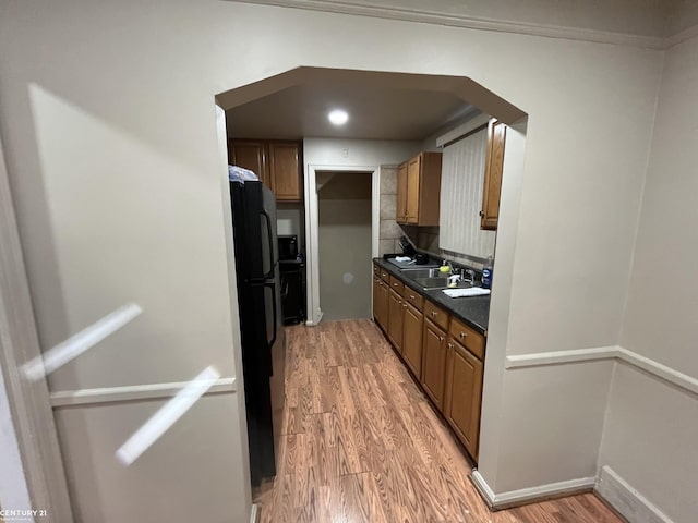 kitchen with arched walkways, freestanding refrigerator, light wood finished floors, brown cabinetry, and dark countertops