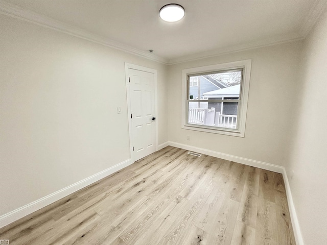 spare room with light wood-type flooring, baseboards, visible vents, and crown molding