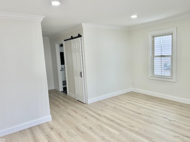 empty room featuring recessed lighting, a barn door, ornamental molding, wood finished floors, and baseboards