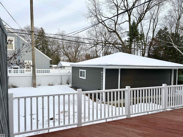 snow covered deck featuring an outbuilding, a detached garage, and fence