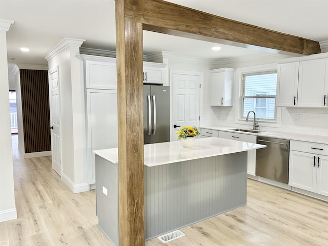 kitchen with light wood finished floors, appliances with stainless steel finishes, backsplash, a sink, and beam ceiling