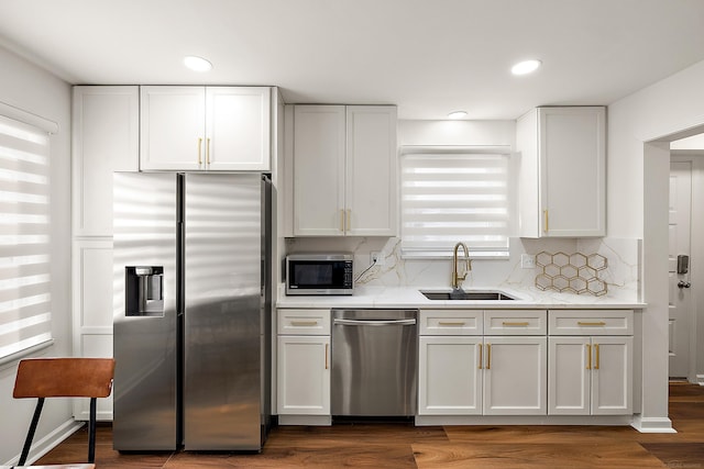 kitchen with white cabinets, dark wood-type flooring, a sink, stainless steel appliances, and backsplash