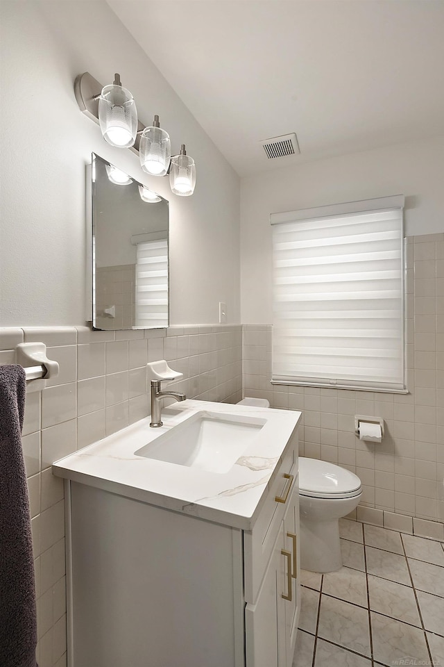 half bath featuring tile patterned flooring, toilet, vanity, visible vents, and tile walls