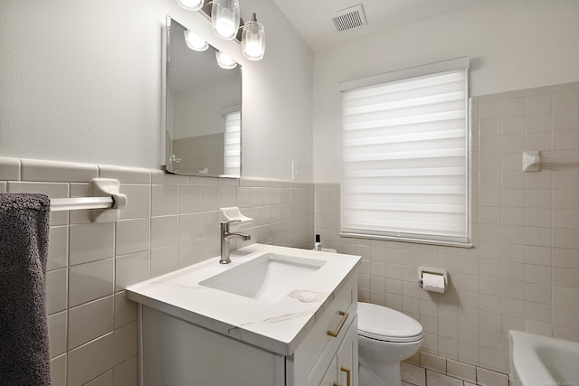 full bath featuring toilet, visible vents, tile walls, vanity, and a tub