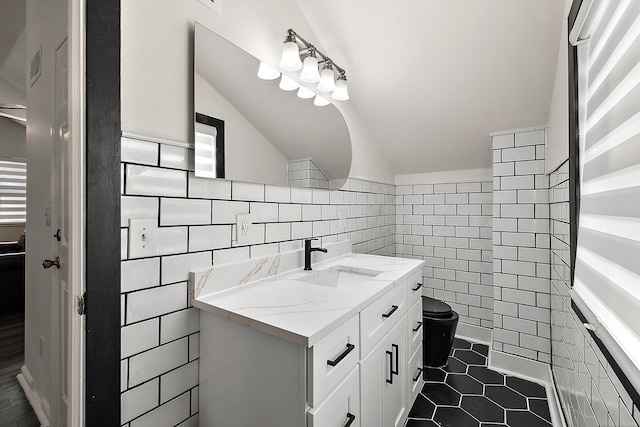 bathroom with toilet, tile patterned floors, vaulted ceiling, vanity, and tile walls